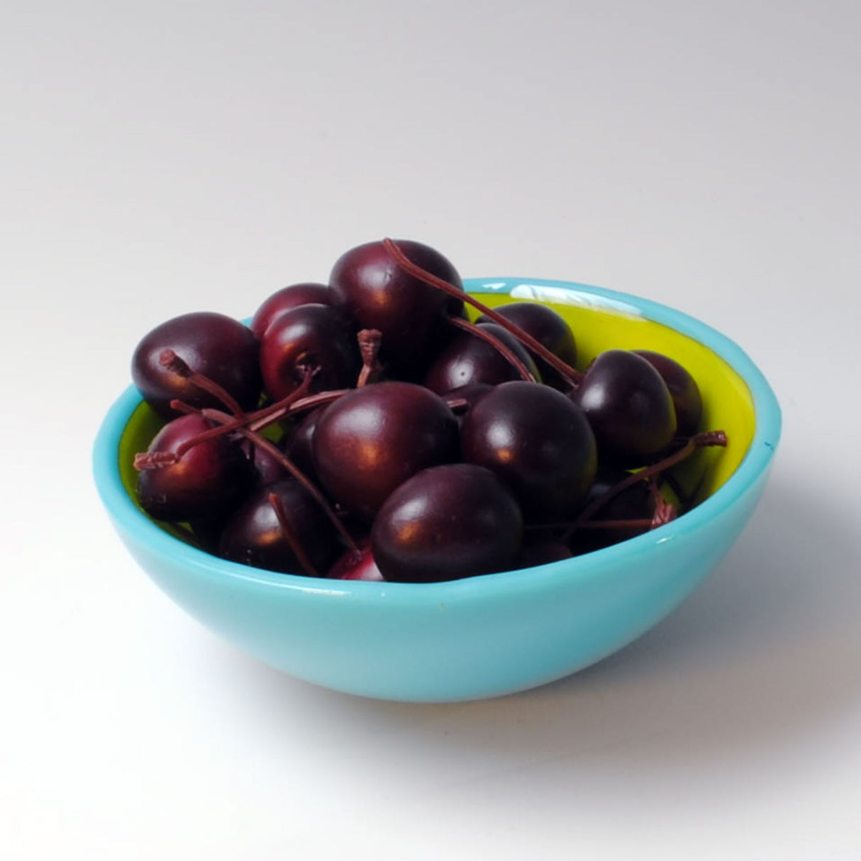 a blue bowl filled with cherries on a white table