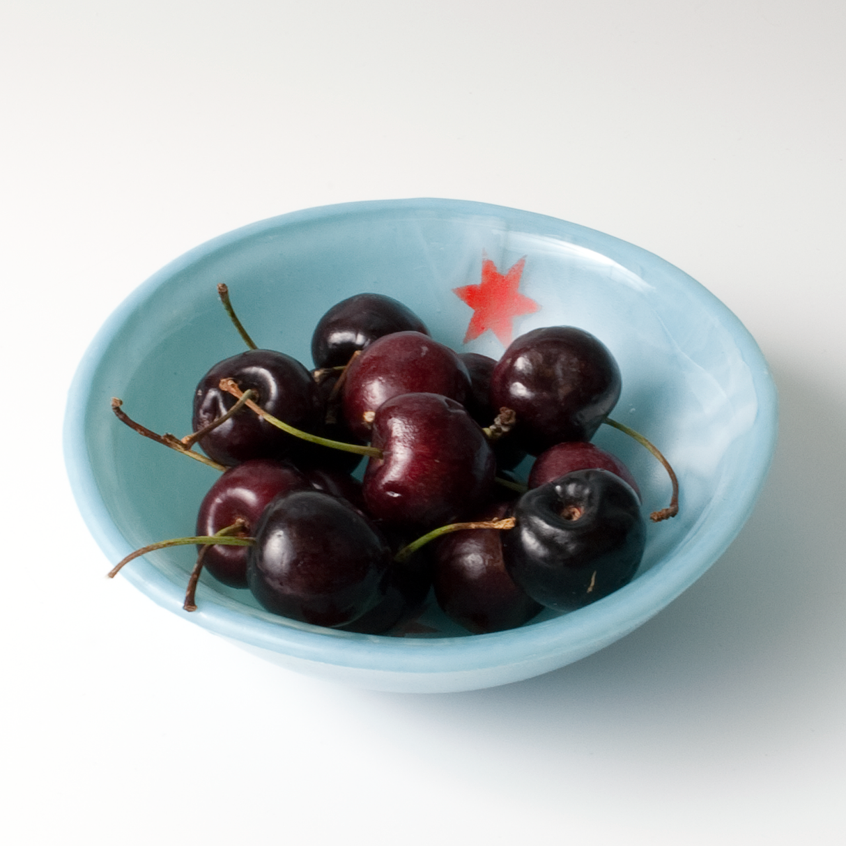 a blue bowl filled with cherries on top of a white table