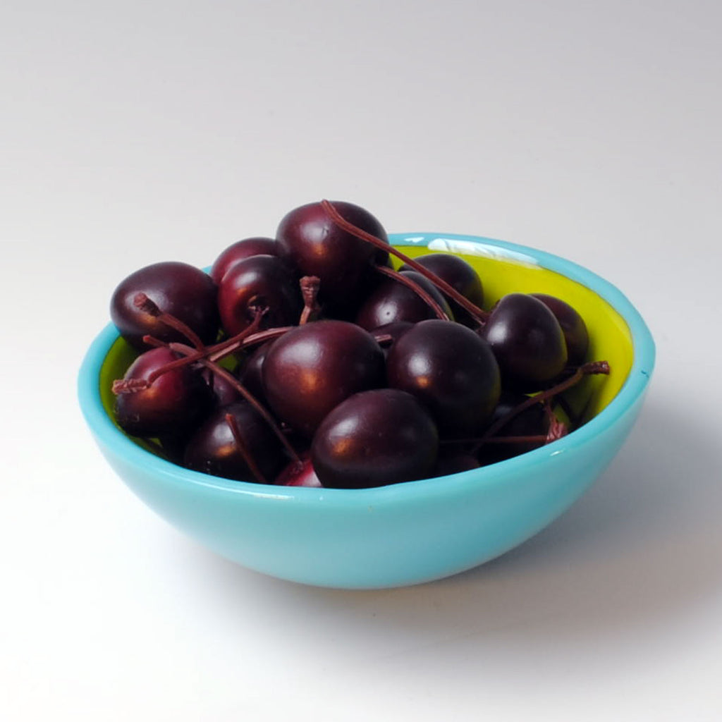 a blue bowl filled with cherries on a white table