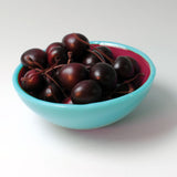 a blue bowl filled with cherries on top of a white table