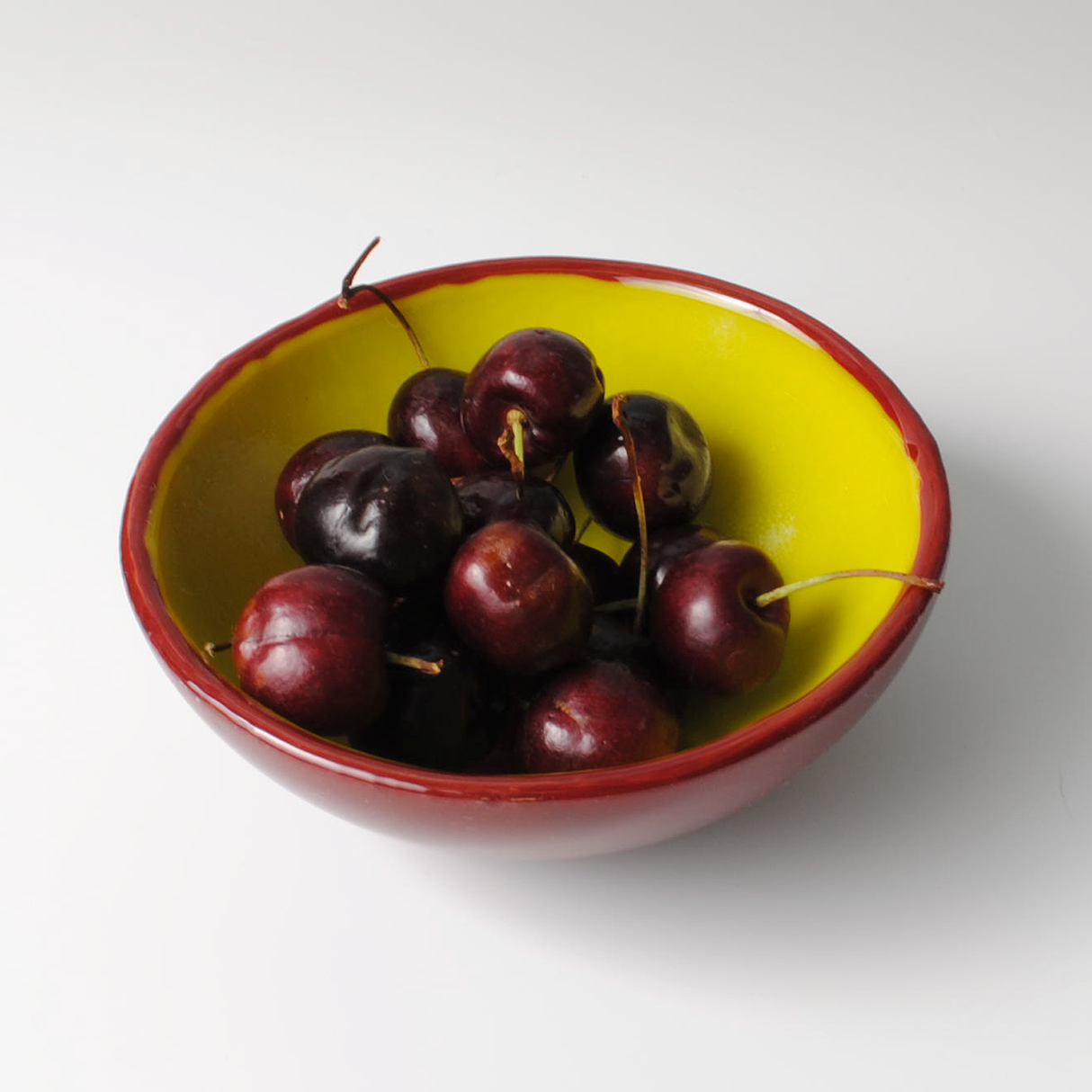 a bowl of cherries on a white surface