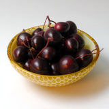a yellow bowl filled with black cherries on a white table